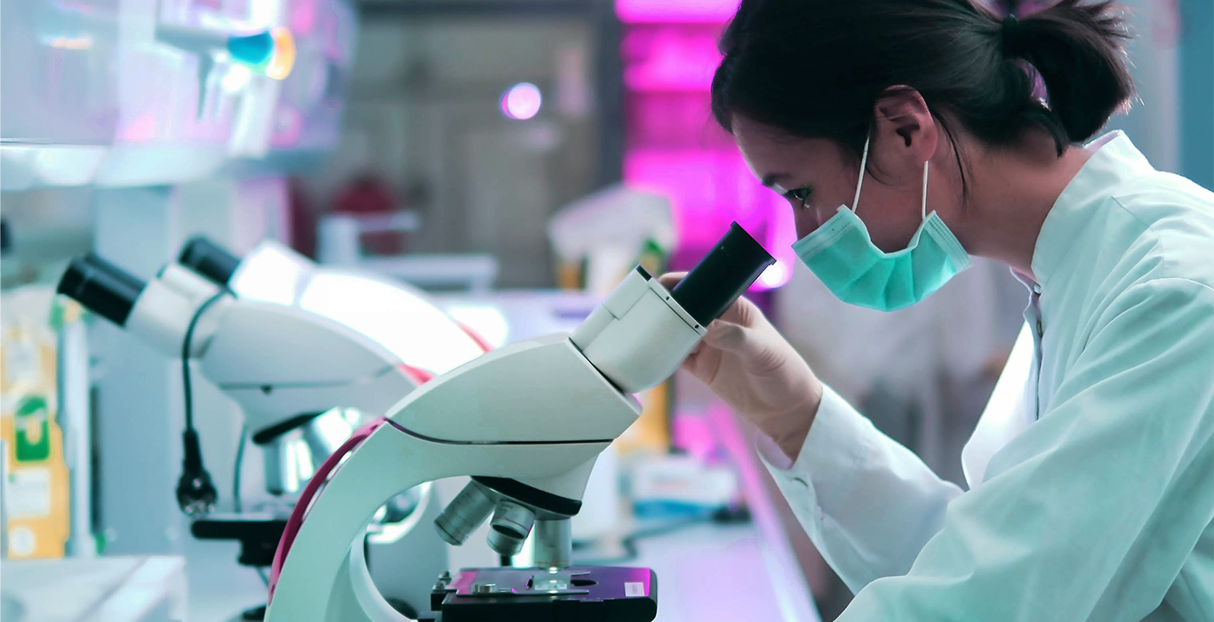 Dynamic Light Scattering - Frau mit Schutzmaske, Laborkittel und Handschuhen schaut in Mikroskop